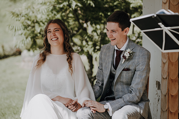 Lachendes Ehepaar (Braut und Bräutigam) sitzen bei freier Trauung und halten sich die Hände.